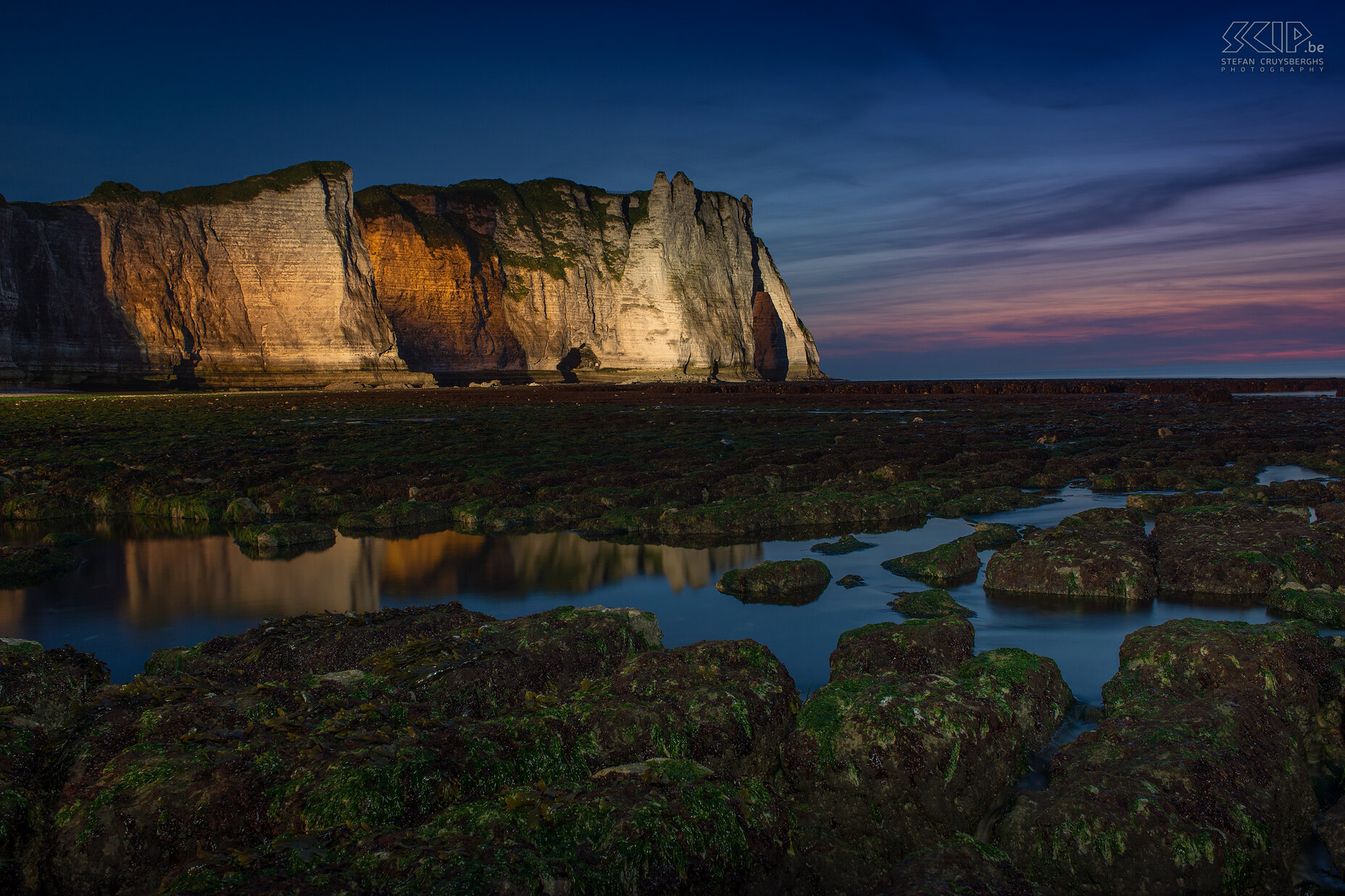 Normandy - Étretat by night The big spotlights lighten up the cliffs with orange and white light during the night. So I looked for some pools and a low viewpoint to get a reflection of the cliffs and I used my small torchlight to lighten up the foreground. The final result was a very colorful night shot of these fantastic cliffs. Stefan Cruysberghs